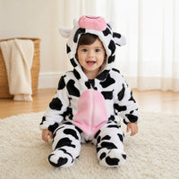 Smiling baby sitting on a rug in a black and white cow costume onesie