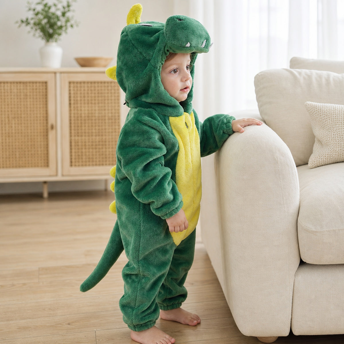 Toddler standing by the sofa in a green dragon onesie with tail